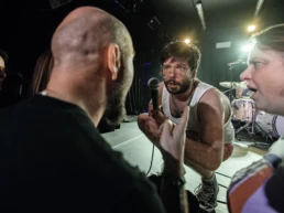 Fríði Djurhuus of Joe & The Shitboys performing at Sonic City Festival in Kortrijk, Belgium. He crouches close to the audience, holding out a microphone as fans gesture and shout back, with intense direct eye contact. Photo by Marvin Anthony.