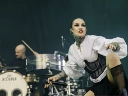 Tatiana Shmayluk of Jinjer performing at Graspop Metal Meeting in Dessel, Belgium. She strikes a powerful pose mid-song, dressed in a white blouse, black corset, and lace stockings, gripping a microphone with intense expression. Drummer visible in background. Photo by Marvin Anthony.